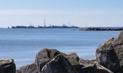 A serene view of a calm lake with distant amusement park rides visible on the horizon, framed by rocky shoreline.