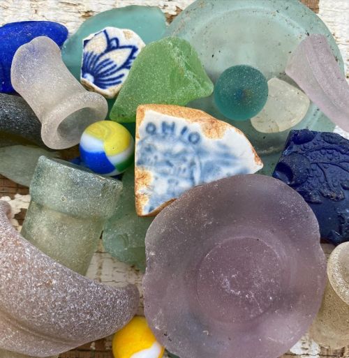 A collection of colorful sea glass, marbles, and pottery shards arranged on a textured surface.