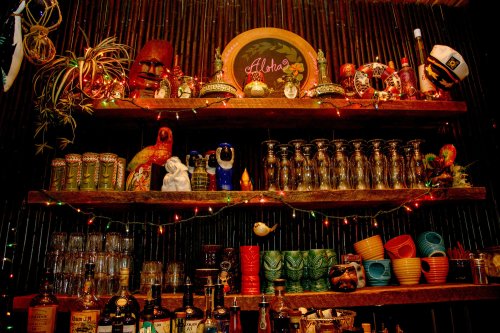 Colorful bar shelves filled with various bottles, glasses, and decorative items, adorned with festive lights.