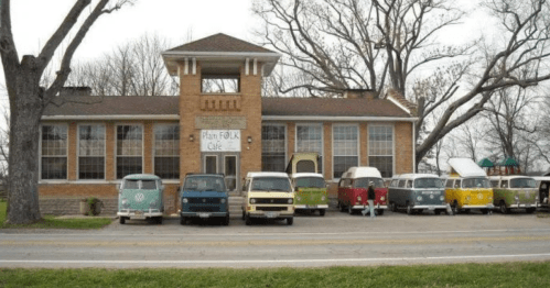 A vintage building with a sign reading "Folk Cafe" and a row of colorful classic vans parked in front.
