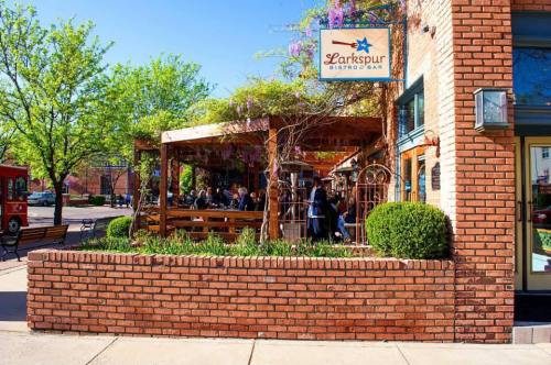 Outdoor dining area of Larkspur Bistro Bar, featuring a wooden pergola and lush greenery, with patrons enjoying their meals.