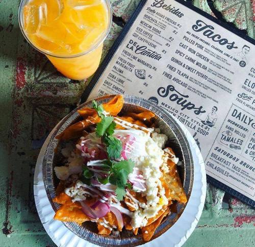 A plate of nachos topped with cheese, onions, and cilantro, alongside a cup of orange drink and a menu.