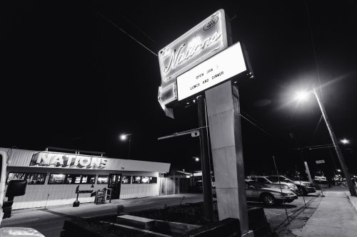 A nighttime view of a diner sign and a restaurant, with cars parked nearby and streetlights illuminating the scene.