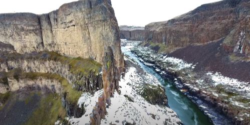 Aerial view of a narrow river winding through steep, rocky cliffs with patches of snow on the ground.