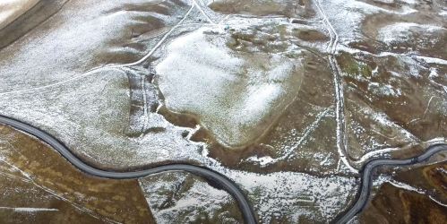 Aerial view of a snow-covered landscape with winding roads and patches of grassland.