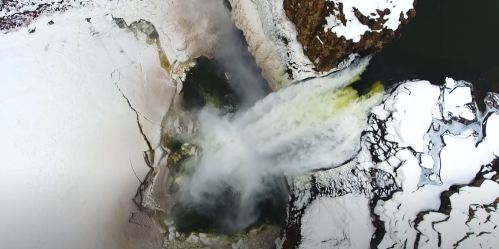 Aerial view of a waterfall cascading into a river, surrounded by snow and ice.