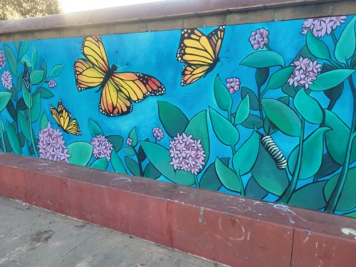 Colorful mural featuring butterflies and flowers against a blue background, with a caterpillar among the greenery.