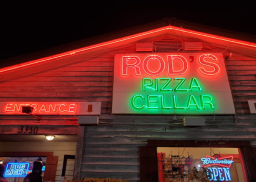 Neon sign for "Rod's Pizza Cellar" illuminated at night, with an entrance arrow and Budweiser sign visible.
