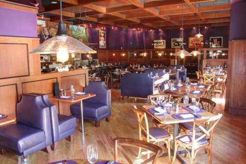A stylish restaurant interior featuring wooden tables, purple accents, and cozy seating arrangements.