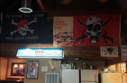 Two pirate-themed banners hang on a wooden wall, alongside a Coors Light sign and a pizza advertisement.