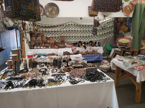 A vibrant display of handmade crafts, including jewelry, drums, and woven items, in a colorful market setting.