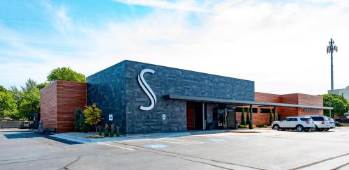 Modern building with a sleek design, featuring a large "S" sign, surrounded by greenery and parked cars.