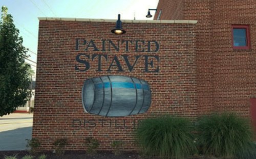 Mural on a brick wall featuring a barrel and the text "Painted Stave Distillery." Green plants in the foreground.