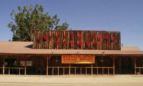 A rustic wooden building with a sign reading "Buffalo Jump Saloon" and a banner for "Ruffalo Jump Steak House."