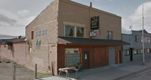 Exterior view of a rustic bar building with a sign reading "Dad's Bar" and a basketball hoop outside.