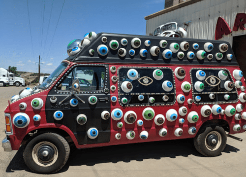 A colorful van covered in various eye designs, parked in a sunny outdoor setting.