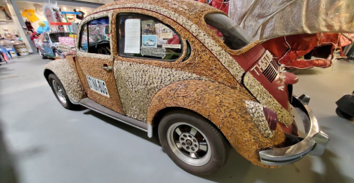 A vintage car covered in colorful corks, displayed in a museum setting.
