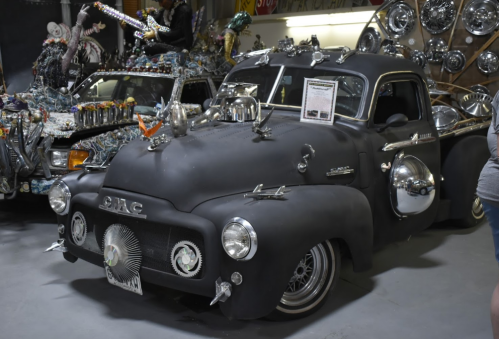 A creatively modified GMC truck with unique decorations and chrome accents, displayed in a quirky automotive exhibit.