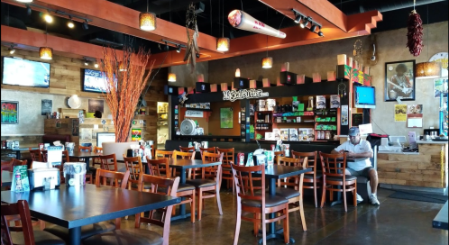 A cozy restaurant interior with wooden decor, tables, and a bar area, featuring a few patrons and wall-mounted TVs.