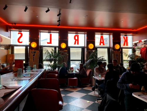 A vibrant restaurant interior with red neon lights, large windows, and patrons seated at tables.