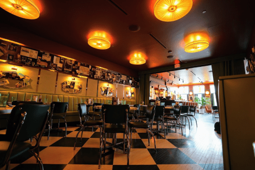 A cozy restaurant interior with checkered floors, green booths, and warm lighting, featuring vintage decor on the walls.