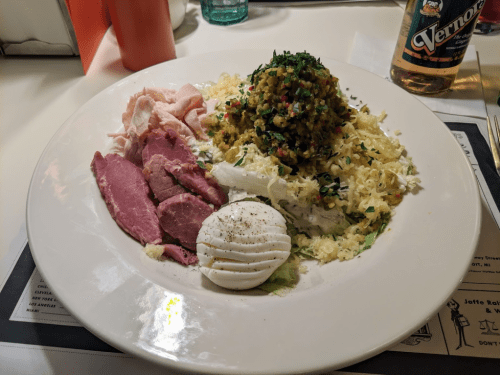 A plate of food featuring sliced meats, a salad with herbs, and a poached egg on a bed of sauerkraut.