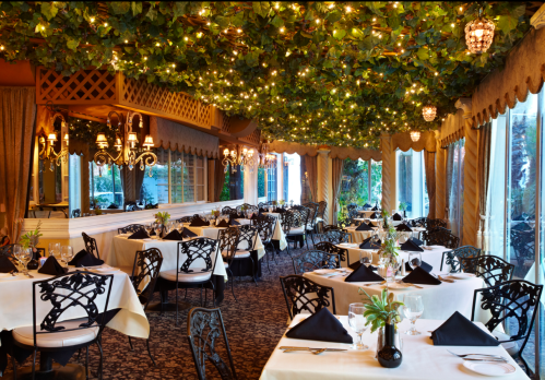 Elegant restaurant interior with tables set for dining, adorned with greenery and soft lighting.