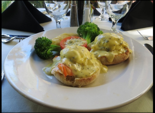 A plate of eggs Benedict with salmon, topped with hollandaise sauce, served with broccoli and tomato slices.