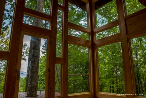 A modern cabin interior with large windows showcasing a lush green forest and a glimpse of water in the distance.