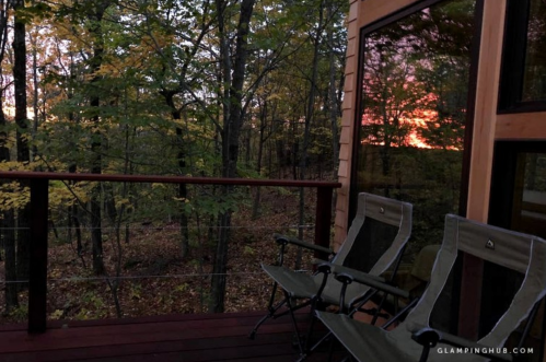 A cozy deck with two chairs overlooks a forest at sunset, with vibrant colors reflecting in the windows.