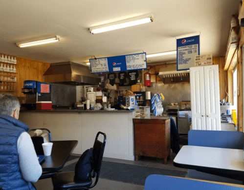 A cozy diner interior with a counter, menu boards, and a customer sitting at a table, enjoying a drink.