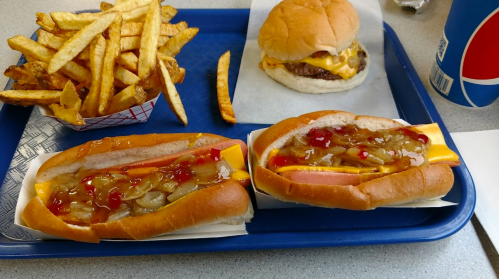 A blue tray with two hot dogs topped with cheese and condiments, a cheeseburger, fries, and a soda.