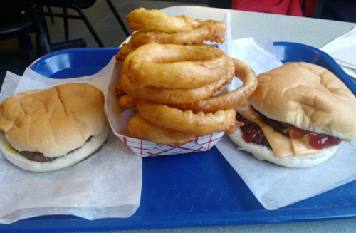 A blue tray with two burgers and a serving of onion rings, all on white paper.