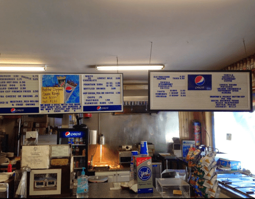 Menu board displaying food and drink options, including burgers, fries, and beverages, in a casual dining setting.