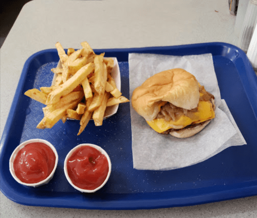 A blue tray with a cheeseburger topped with onions, fries, and two cups of ketchup.