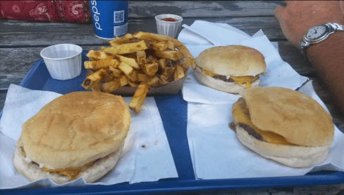A tray with three cheeseburgers and a basket of fries, accompanied by dipping sauces and a can of Pepsi.