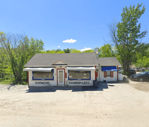 A small, charming hamburger restaurant with a sign reading "Harmons Hamburgers," surrounded by trees and a clear blue sky.