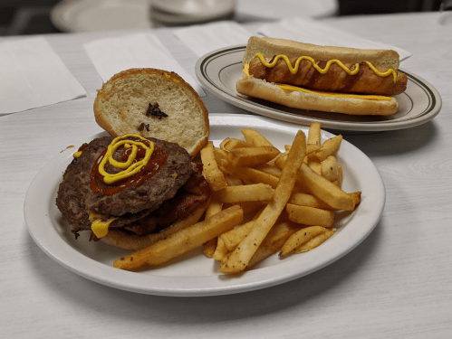 A plate with a burger topped with ketchup and mustard, fries, and a hot dog with mustard on a separate plate.