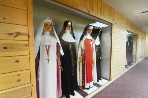 Display of mannequins dressed in various nun habits, arranged in a hallway with wooden paneling.