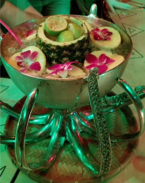A large, decorative bowl filled with fruit, ice, and flowers, resting on a unique metal stand with a greenish glow.