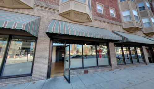 A storefront with striped awnings and an open door, located in a brick building on a city street.