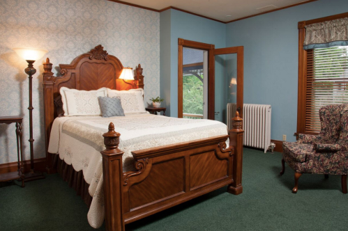 Cozy bedroom featuring a wooden bed, floral armchair, and vintage decor with blue walls and green carpet.