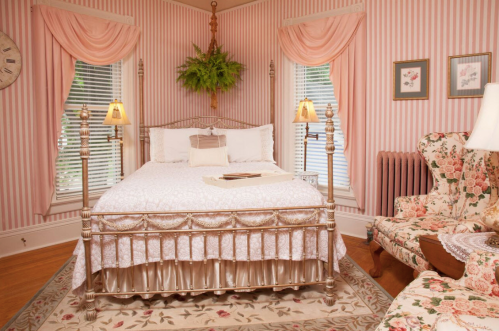 Cozy bedroom with a floral theme, featuring a metal bed, patterned armchair, and soft pink striped walls.