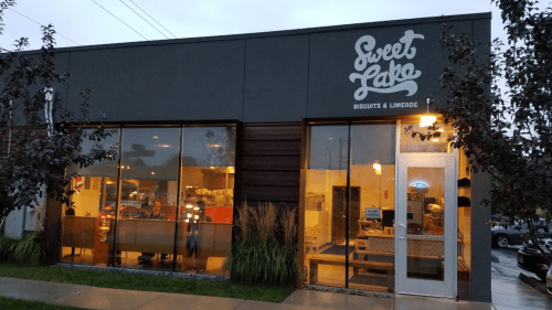 Exterior of Sweet Lake Biscuits & Limeade, featuring large windows and a modern design, on a cloudy evening.
