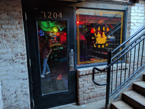A dimly lit entrance to a bar with colorful lights and a sign reading "Laka Lono," surrounded by brick walls.