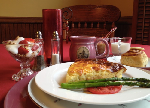 A beautifully set table with a breakfast spread, including a frittata, asparagus, yogurt parfait, and a cinnamon roll.
