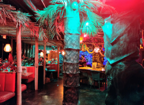 Tropical-themed restaurant interior with palm trees, colorful lighting, and cozy seating areas.