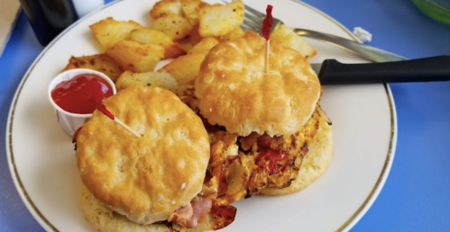 Two biscuit sandwiches filled with chicken and ham, served with crispy potato wedges and a side of ketchup.