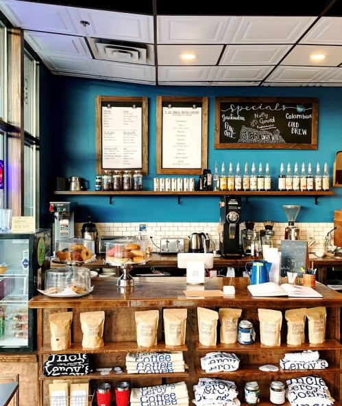 Cozy coffee shop interior with a wooden counter, menu boards, coffee equipment, and baked goods on display.