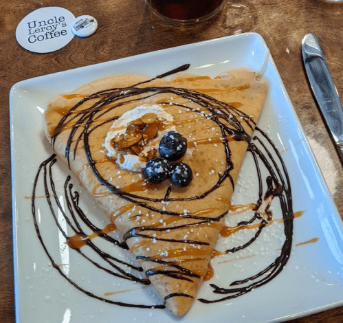 A delicious crepe topped with whipped cream, blueberries, caramel drizzle, and chocolate sauce on a white plate.